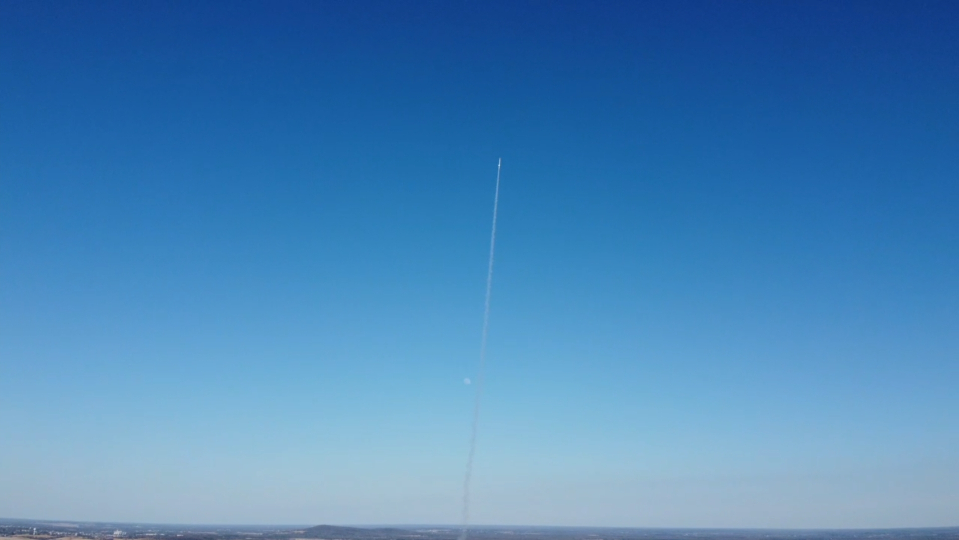 A solid rocket motor climbing through a clear blue sky, trailing a long exhaust plume